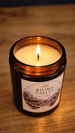 Lit Kilima Valley vegan soy wax candle in an amber glass jar, showing the flame and cosy cashmere and soft amber label on a wooden surface.
