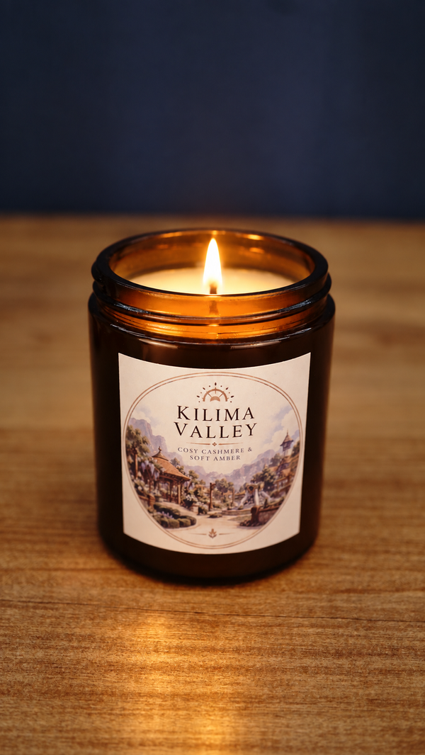 Front view of a lit Kilima Valley vegan soy candle in amber glass, with a warm flame and cosy cashmere and soft amber fragrance label.