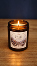 Front view of a lit Kilima Valley vegan soy candle in amber glass, with a warm flame and cosy cashmere and soft amber fragrance label.