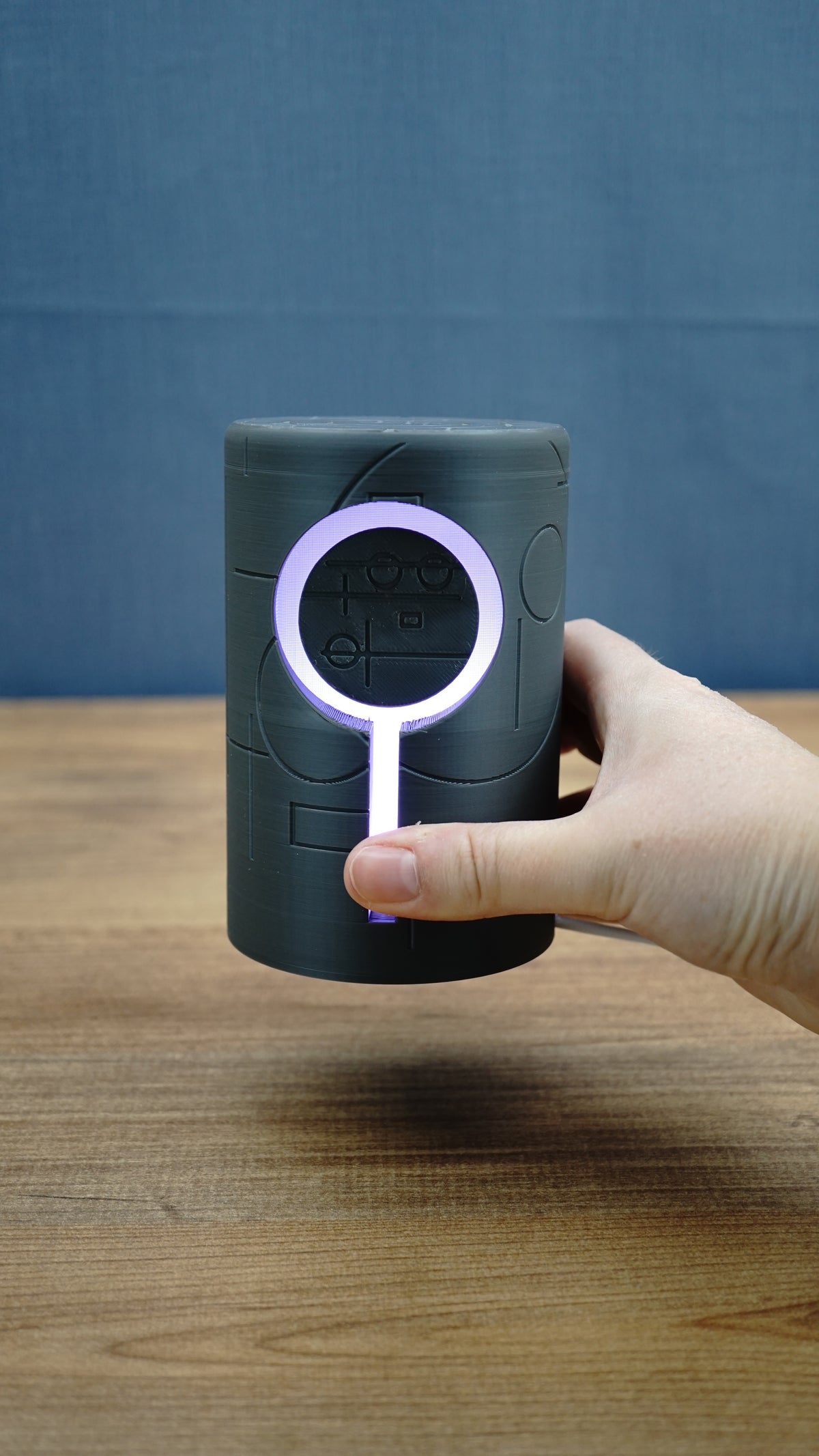 Hand holding the 12cm Knowledge Stone RGB lamp for scale, with the circular LED ring and vertical light strip illuminated pale purple.