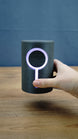 Hand holding the 12cm Knowledge Stone RGB lamp for scale, with the circular LED ring and vertical light strip illuminated pale purple.