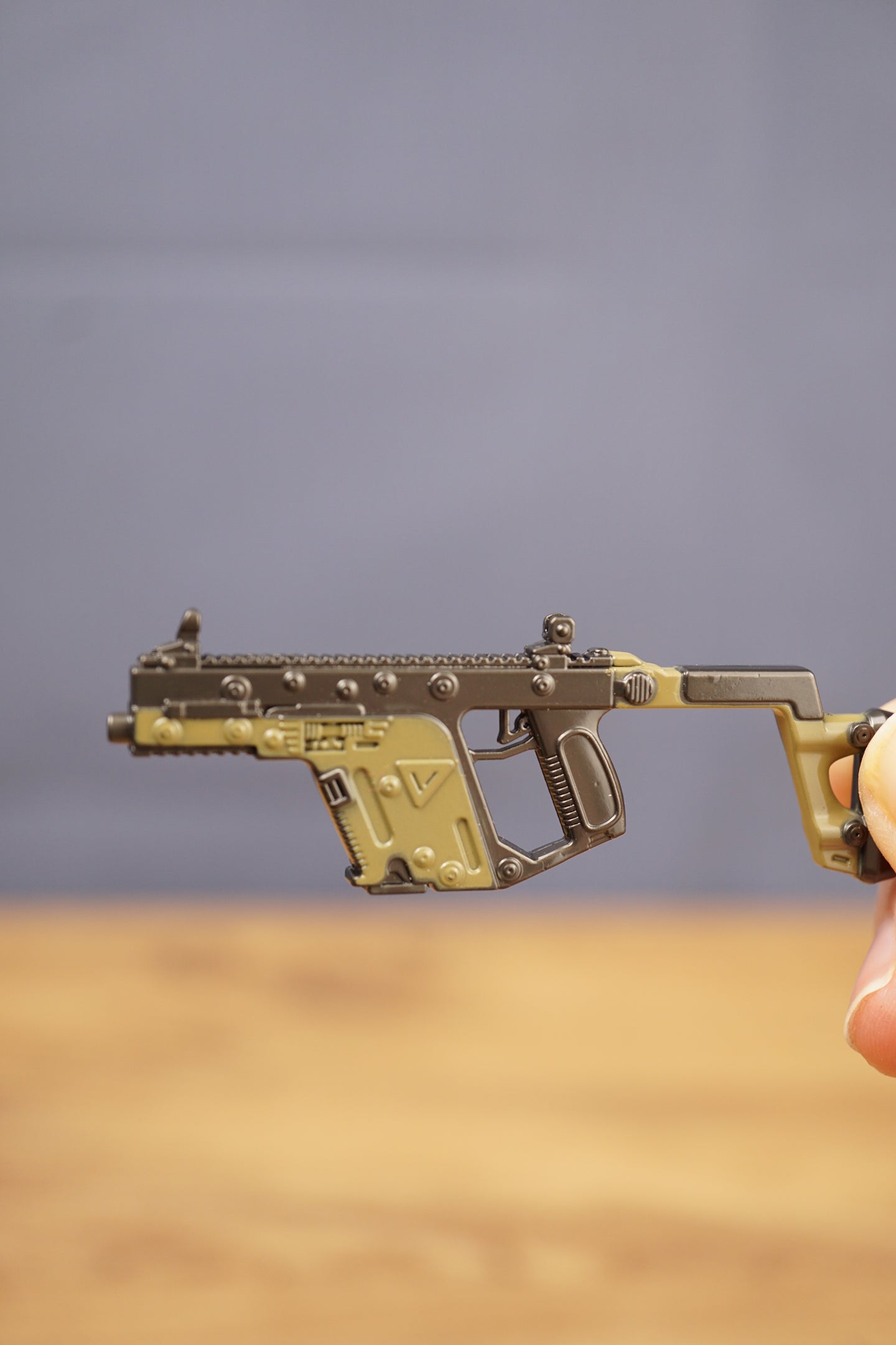 Close-up KRISS Vector style miniature SMG keychain held by hand, showing detailed rail, grip and tactical olive green body finish