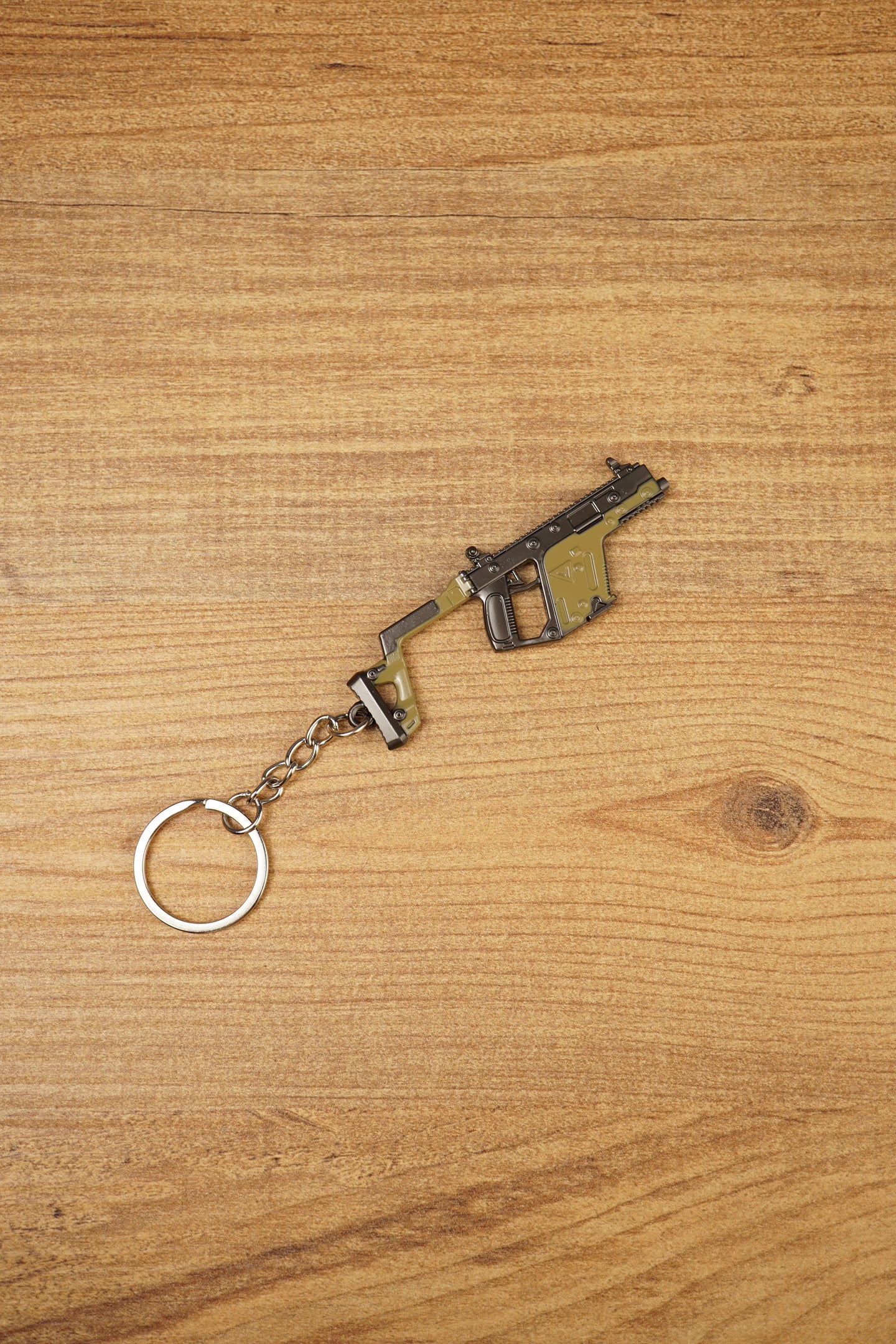 Angled KRISS Vector style SMG keyring on wood showing olive green and black details, a compact collectible for tactical shooter gamers
