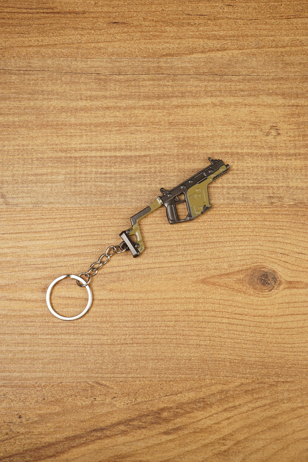 Angled KRISS Vector style SMG keyring on wood showing olive green and black details, a compact collectible for tactical shooter gamers