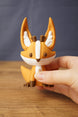Large Ancient Kitsuu collectible held in hand showing orange fox design, white face stripe, brown antlers and curled tail