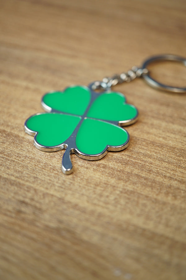 Close-up angled view of a green four leaf clover keychain with polished silver edging, metal keyring, and heart-shaped clover leaves