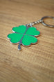 Close-up angled view of a green four leaf clover keychain with polished silver edging, metal keyring, and heart-shaped clover leaves