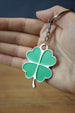 Handheld four leaf clover keychain with green enamel-style leaves, silver trim, and attached chain and ring for keys or bags.