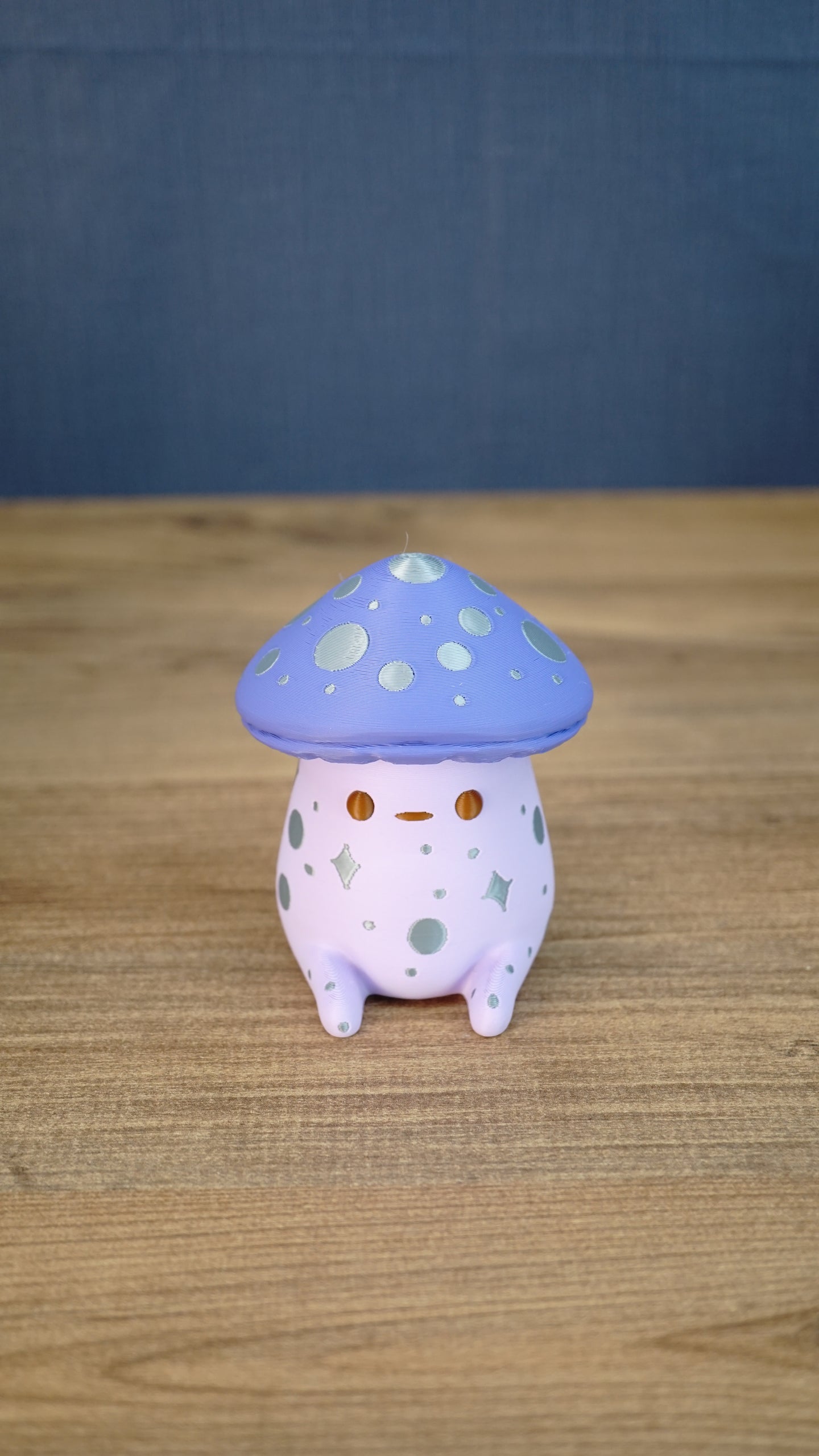Front view of a Madrinas Fun Guy figurine with a lavender mushroom cap, silver spots, orange eyes, and a pale pink body.