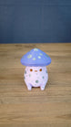 Front view of a Madrinas Fun Guy figurine with a lavender mushroom cap, silver spots, orange eyes, and a pale pink body.
