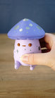 Close-up of a Madrinas Fun Guy figurine being held, showing its lavender cap, silver spots, orange eyes, and pale pink body details.