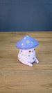 Side view of the Madrinas Fun Guy figurine showing its lavender cap, silver spots, pale pink body, and small rounded feet.