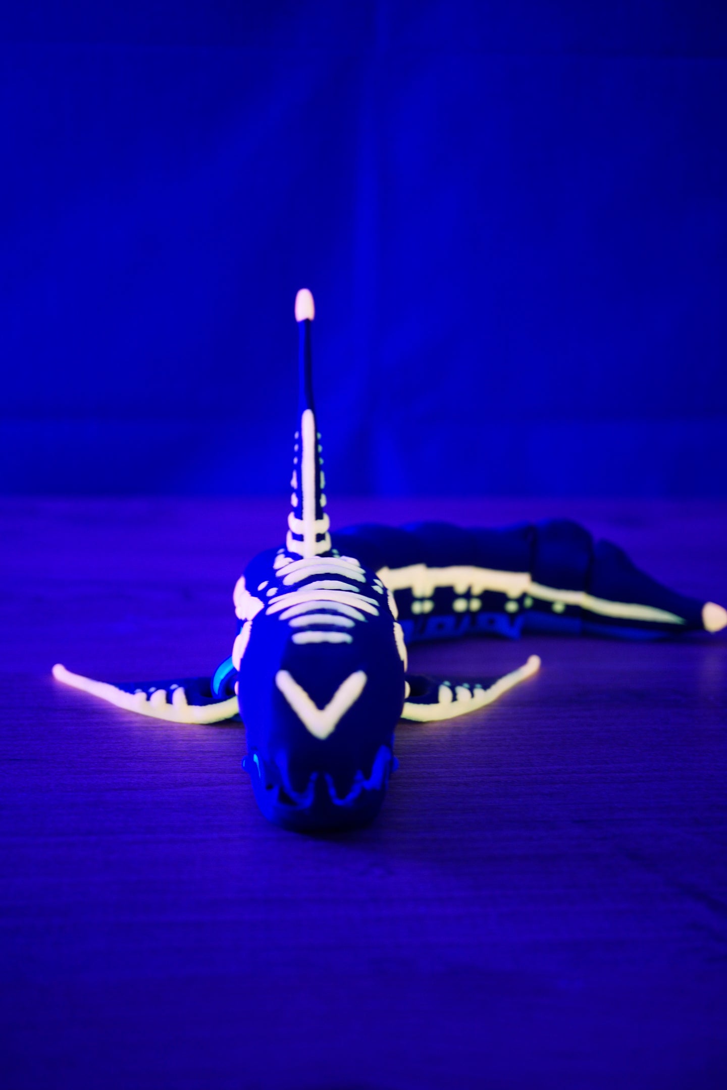 Front-facing Marrowbreach inspired creature figure under blue UV lighting, with glowing facial markings, wide fins and long segmented body behind.