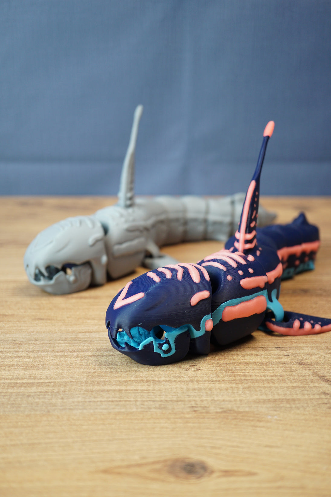 Angled front view of Marrowbreach inspired collectible figure with dark blue body, coral red markings, light blue jaw detail and segmented tail.