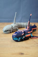 Angled front view of Marrowbreach inspired collectible figure with dark blue body, coral red markings, light blue jaw detail and segmented tail.