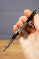Black AKM-style metal rifle keyring held in hand with chain and ring visible, compact collectible for tactical shooter fans