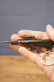 AUG-style metal gun keyring held in hand to show scale, featuring tactical scope, green body, magazine detail and keychain ring