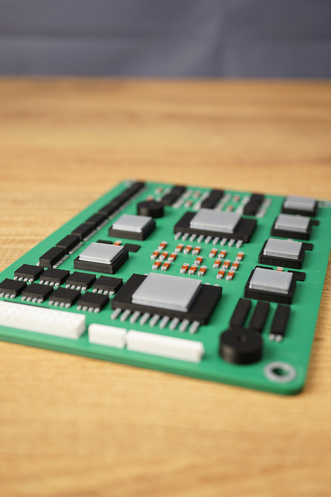 Low-angle close-up of a military circuit board replica on a wooden desk, focusing on raised chips, silver modules, white ports, and detailed components.