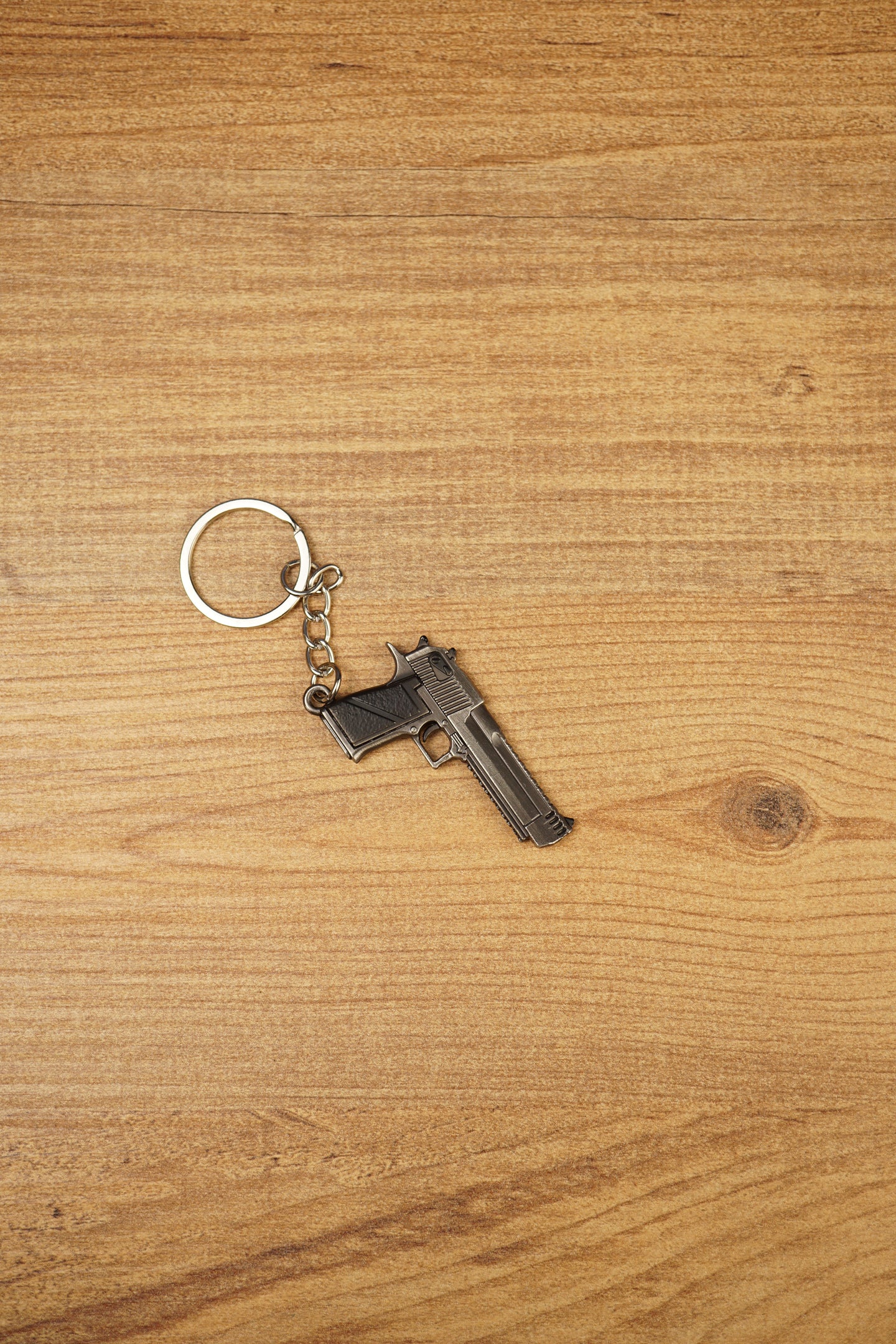 Miniature Deagle pistol keychain displayed on a wooden tabletop with black grip detail, gunmetal body and attached keyring chain
