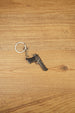 Miniature Deagle pistol keychain displayed on a wooden tabletop with black grip detail, gunmetal body and attached keyring chain