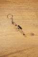 Mini tactical rifle keychain with tan body, black scope and metal keyring, shown diagonally on wood for FPS gamer accessory listing