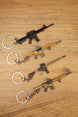 Angled display of four tactical rifle keychains on a wooden background showing different FPS gamer accessory styles.
