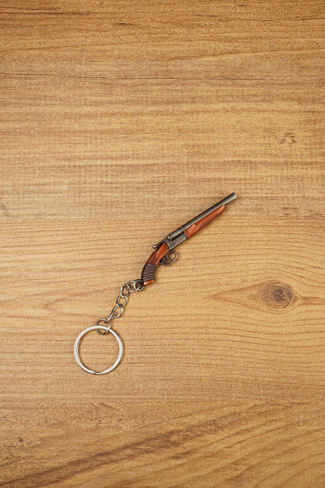 Mini double-barrel shotgun keychain displayed diagonally on wood, featuring gunmetal barrels, brown stock detail and silver keyring