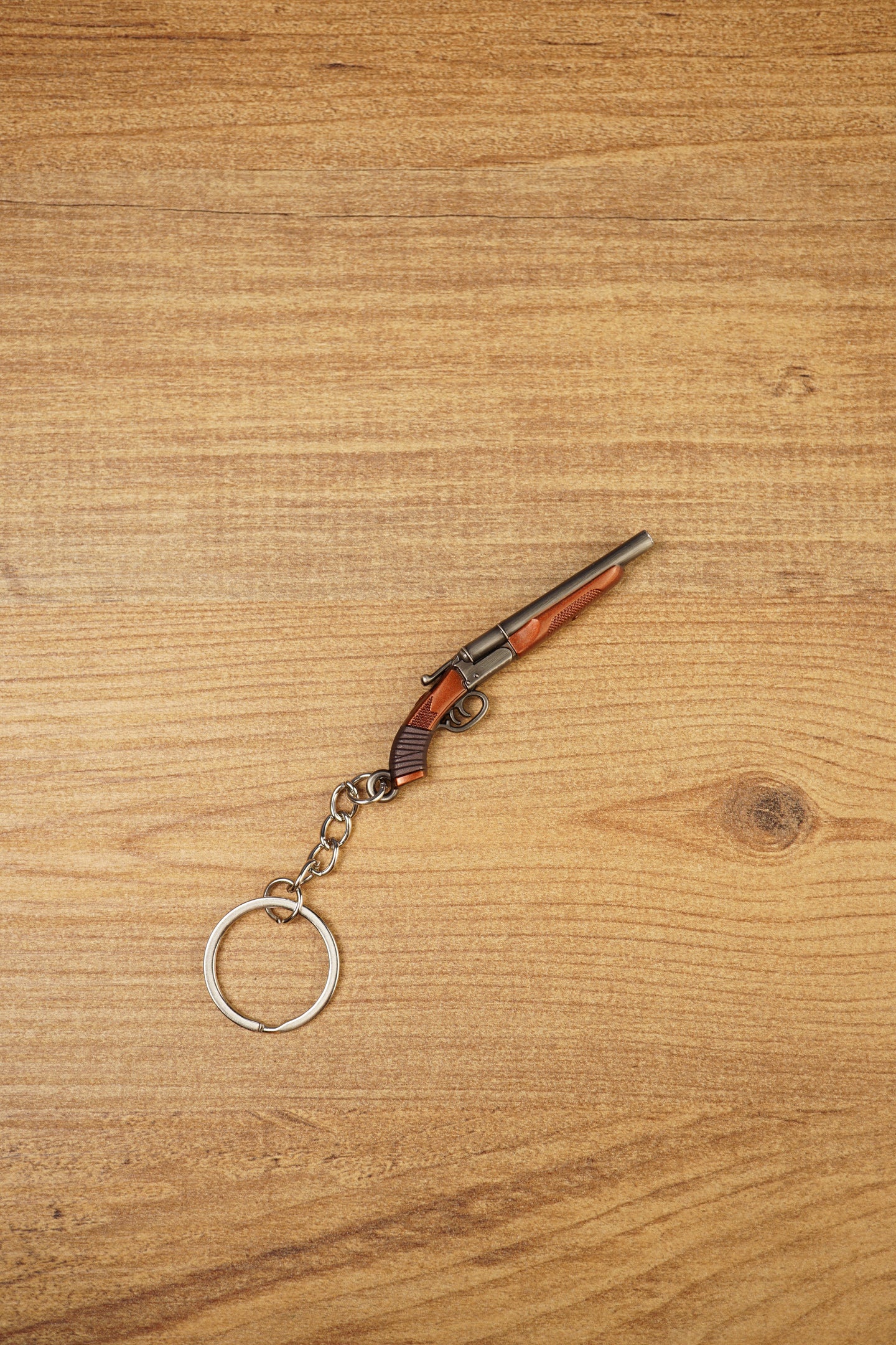 Mini double-barrel shotgun keychain displayed diagonally on wood, featuring gunmetal barrels, brown stock detail and silver keyring