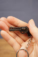 Hand holding a mini tactical revolver keychain with black grip and metal keyring, ideal as a gamer gift or backpack accessory