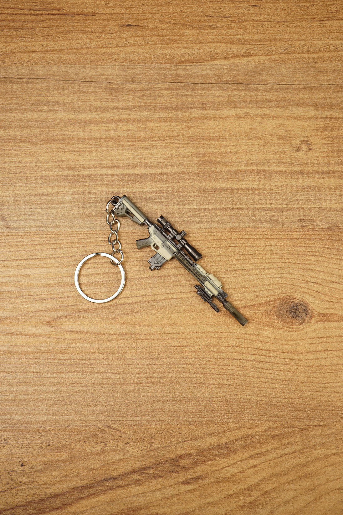 Miniature SR-25 DMR keyring displayed diagonally on a wooden background, featuring tan and black tactical styling with metal chain and ring.