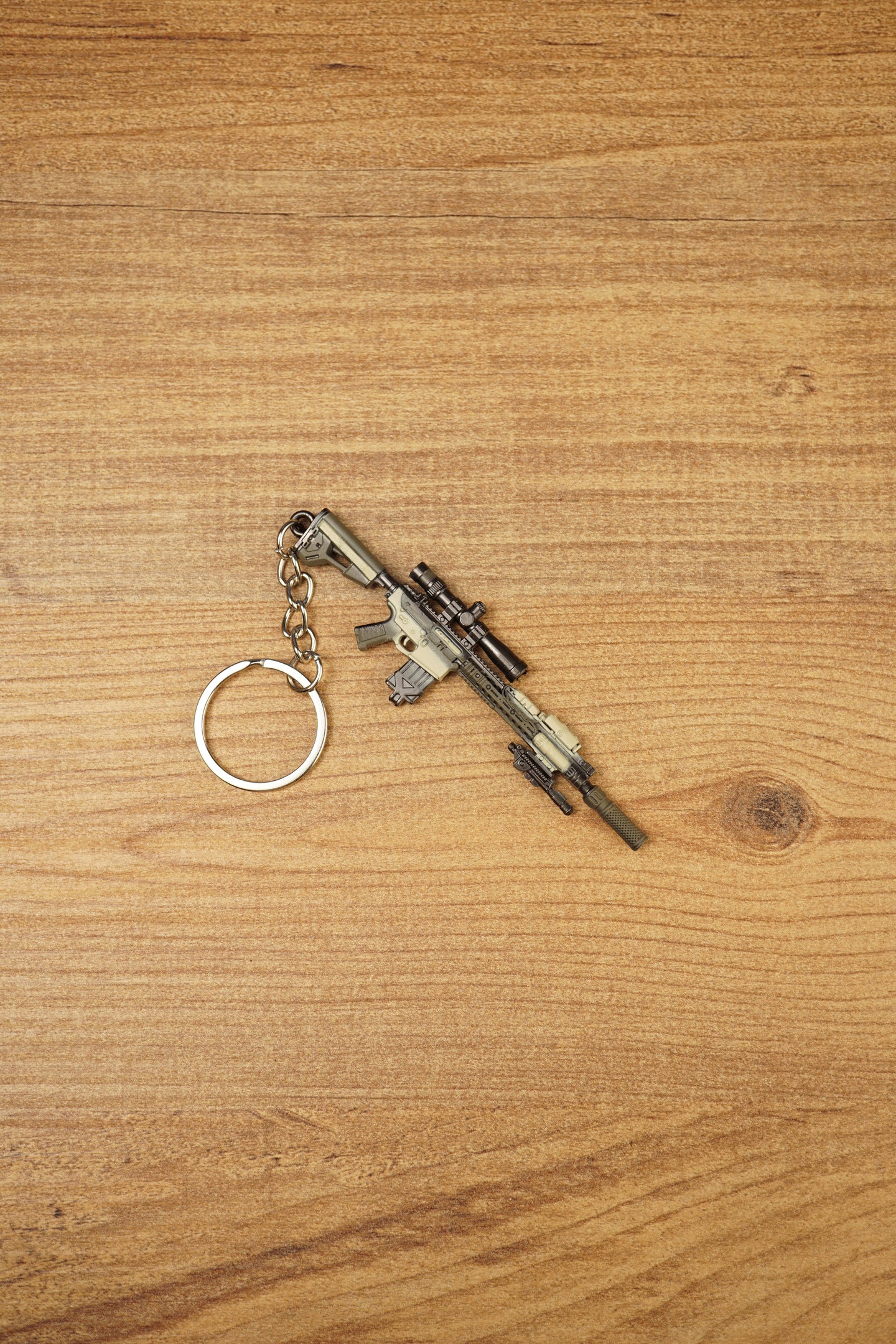 Miniature SR-25 DMR keyring displayed diagonally on a wooden background, featuring tan and black tactical styling with metal chain and ring.
