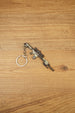 Miniature SR-25 DMR keyring displayed diagonally on a wooden background, featuring tan and black tactical styling with metal chain and ring.