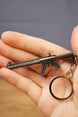 MK47-style metal rifle keychain held in hand to show scale, with detailed finish, chain attachment and round keyring loop