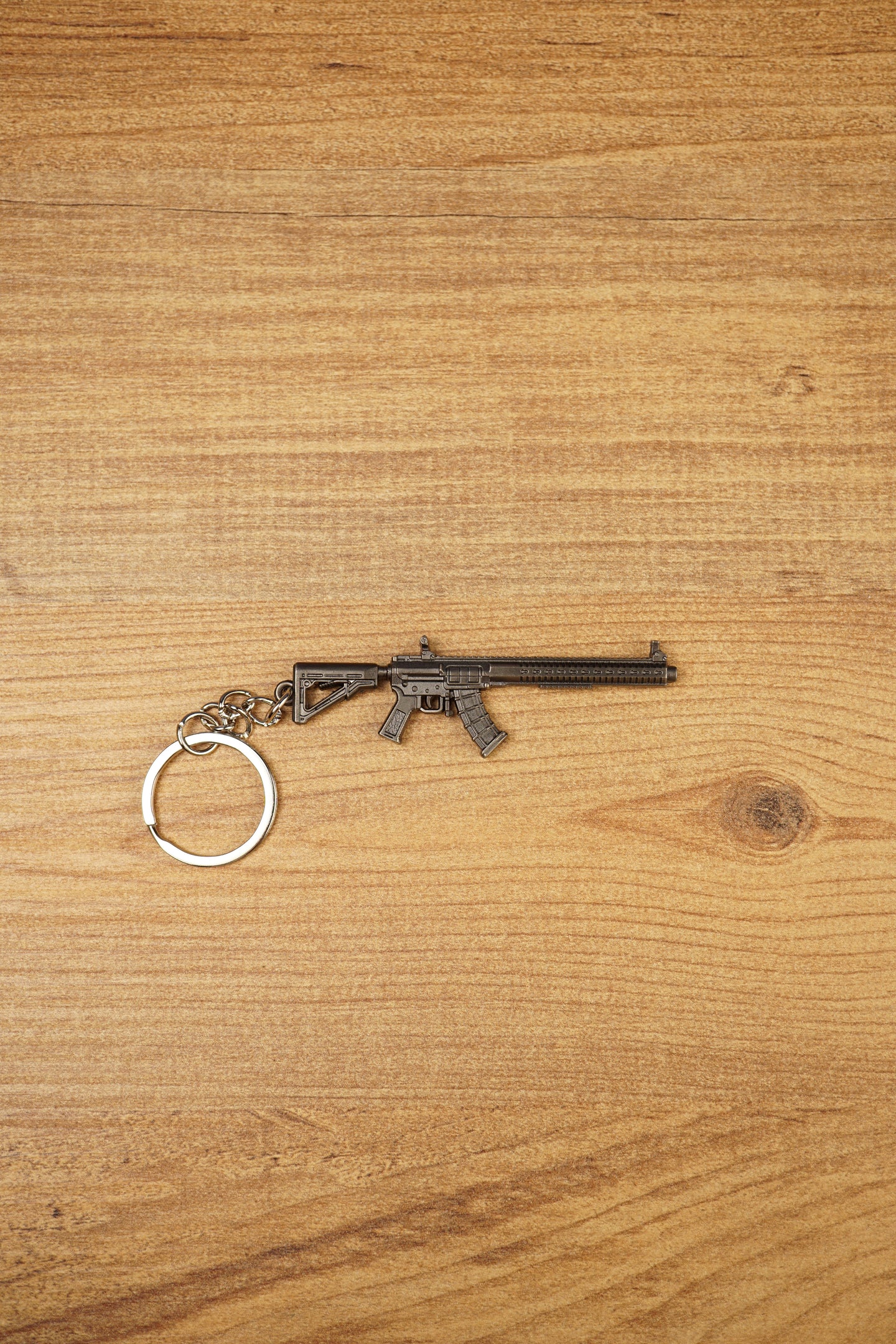 MK47 metal rifle keyring laid flat on a wooden surface, showing the full miniature tactical design with chain and split ring