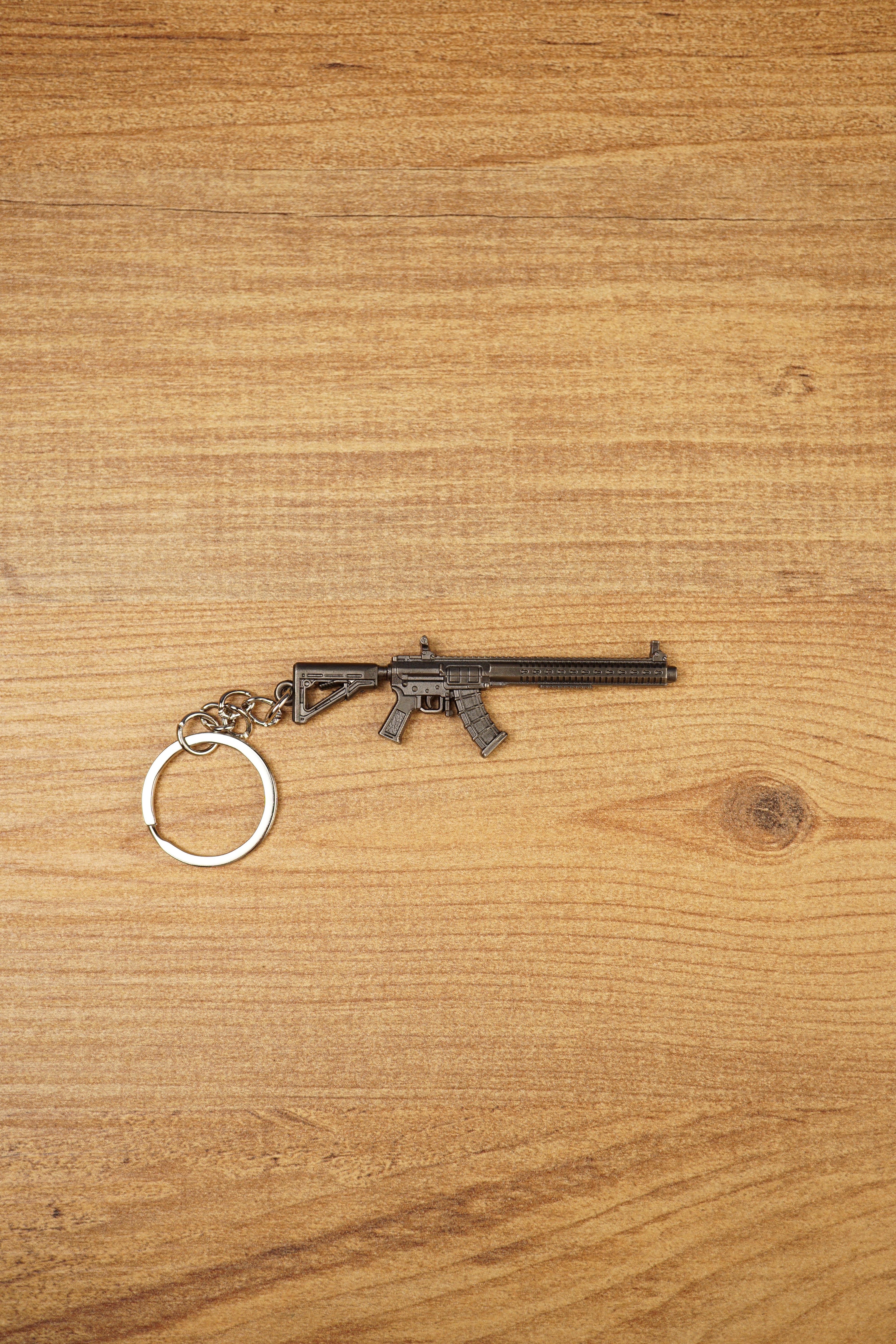 MK47 metal rifle keyring laid flat on a wooden surface, showing the full miniature tactical design with chain and split ring