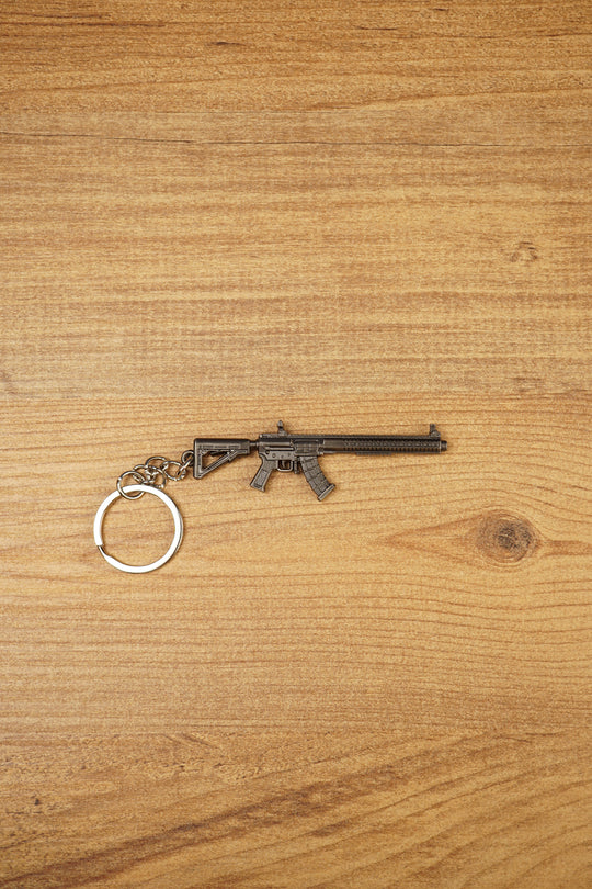 MK47 metal rifle keyring laid flat on a wooden surface, showing the full miniature tactical design with chain and split ring