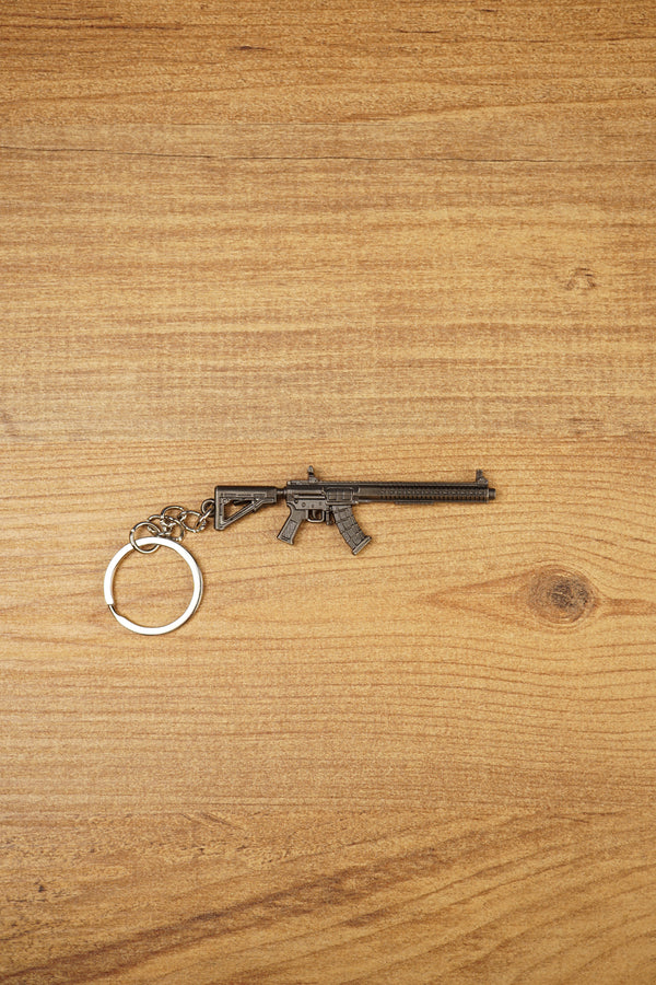 MK47 metal rifle keyring laid flat on a wooden surface, showing the full miniature tactical design with chain and split ring