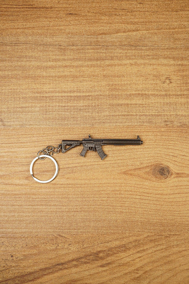 MK47 metal rifle keyring laid flat on a wooden surface, showing the full miniature tactical design with chain and split ring