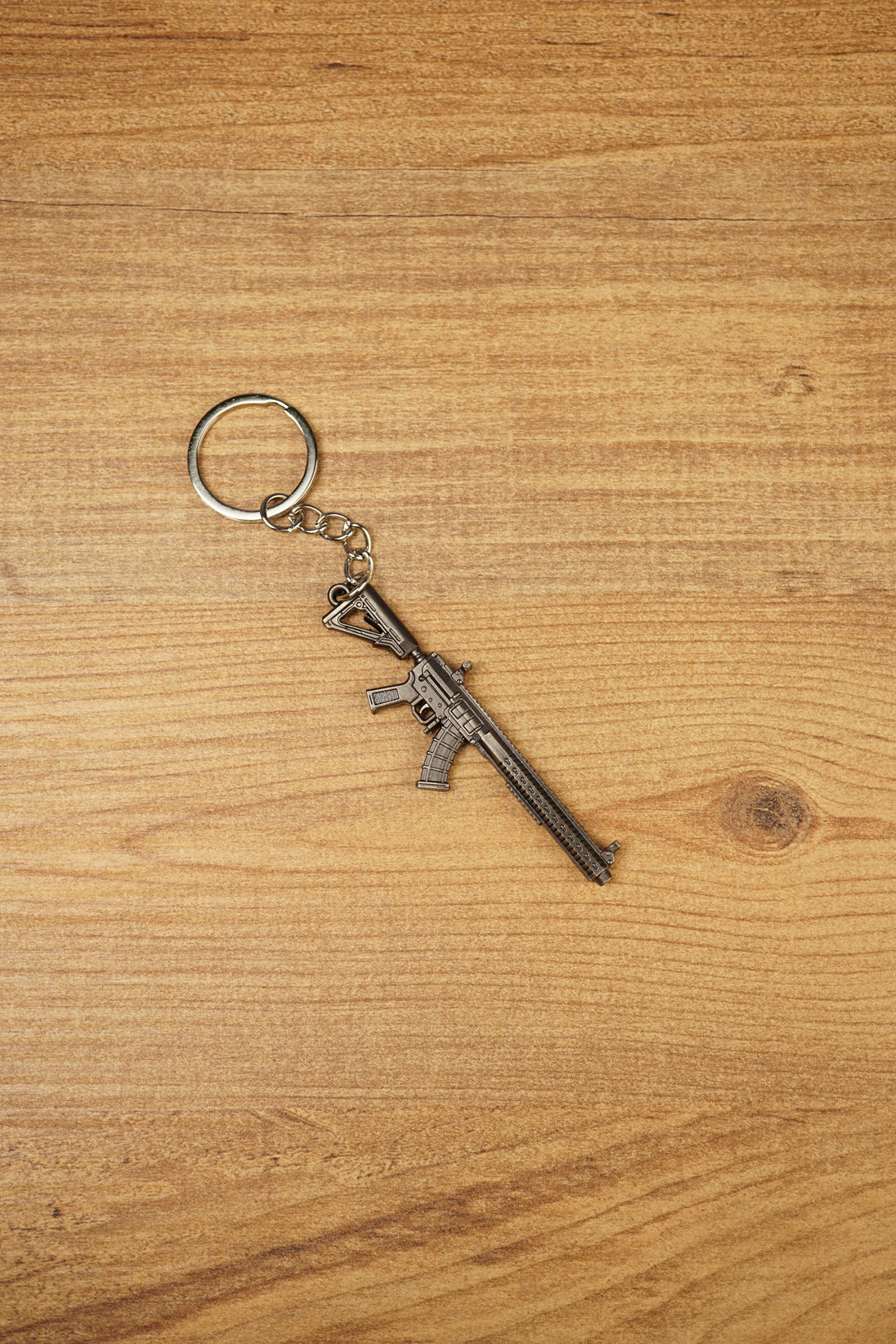 Detailed metal rifle keyring with tactical MK47-style shape, chain and key loop displayed on a wooden background for collectors