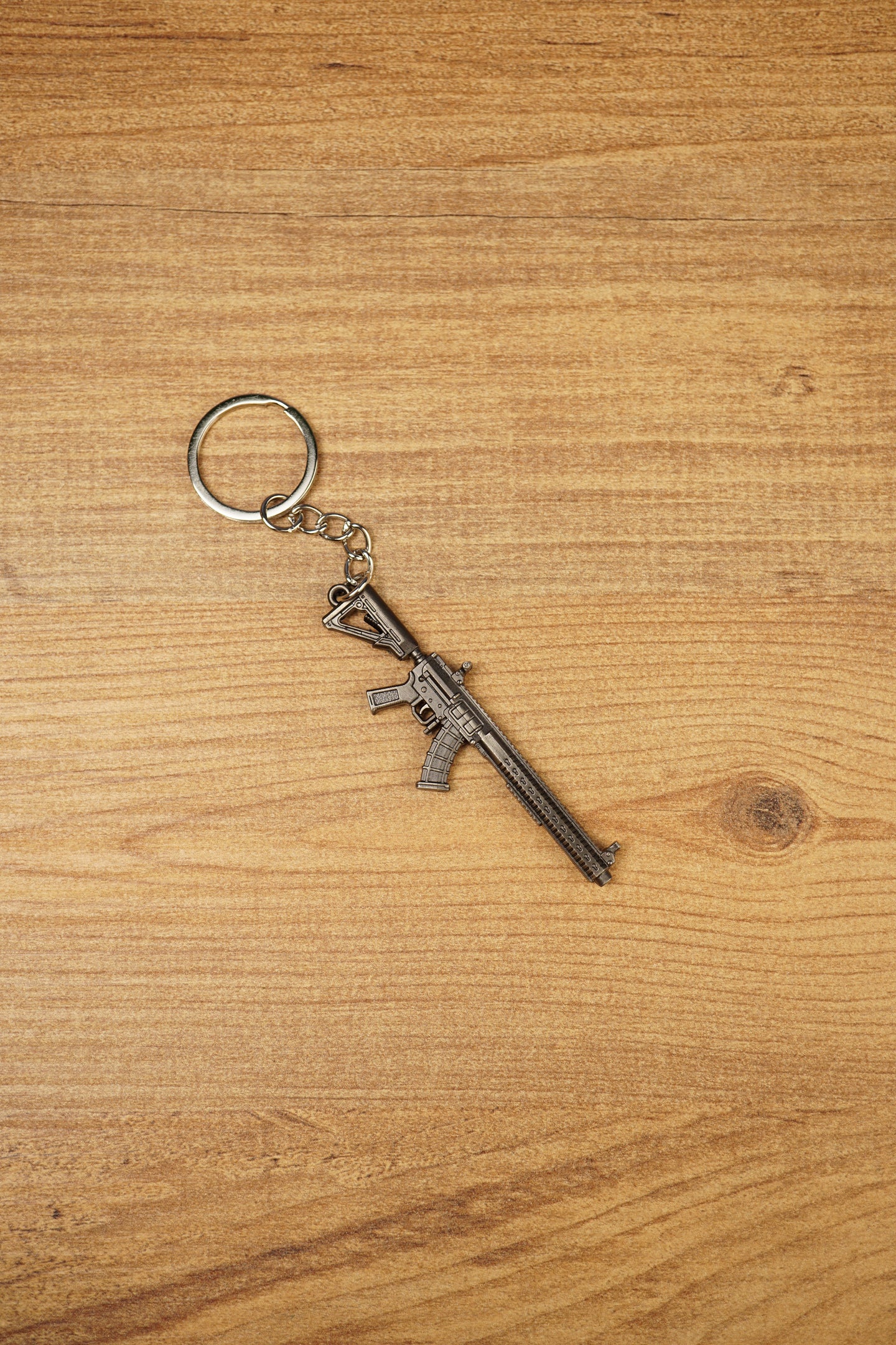 Detailed metal rifle keyring with tactical MK47-style shape, chain and key loop displayed on a wooden background for collectors