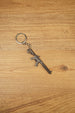 Detailed metal rifle keyring with tactical MK47-style shape, chain and key loop displayed on a wooden background for collectors