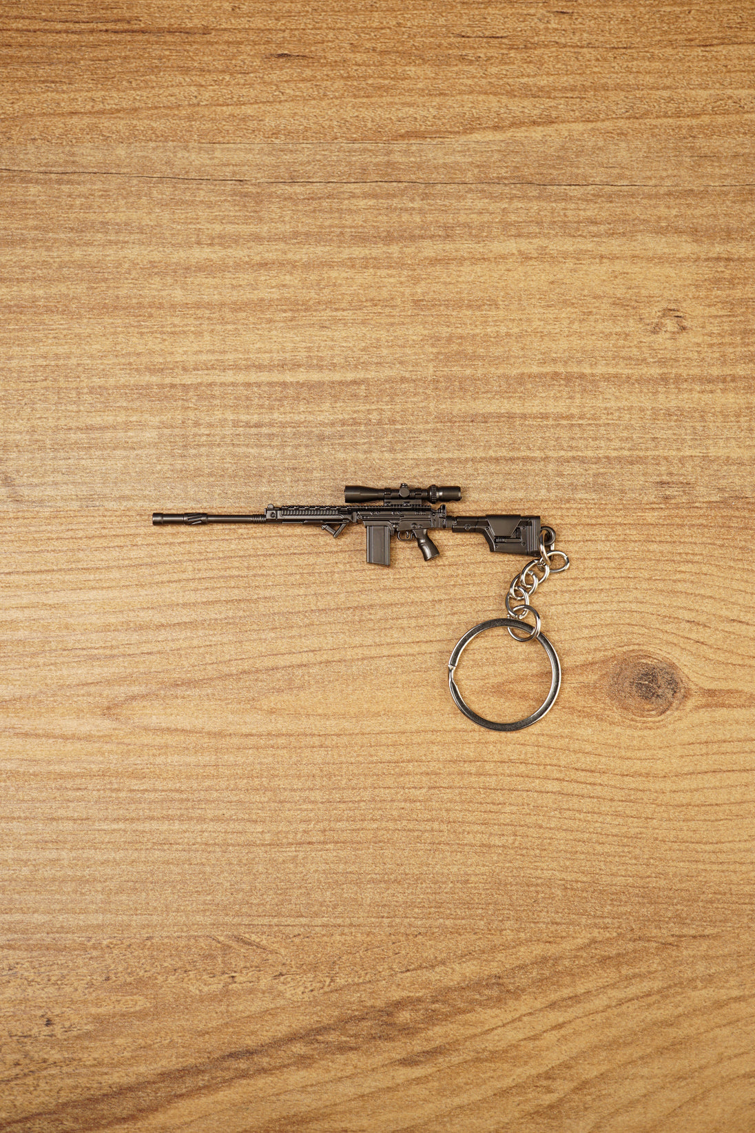 Modded SA58 FAL rifle keychain with scope-style detail, dark gunmetal finish and metal keyring attachment on wooden background