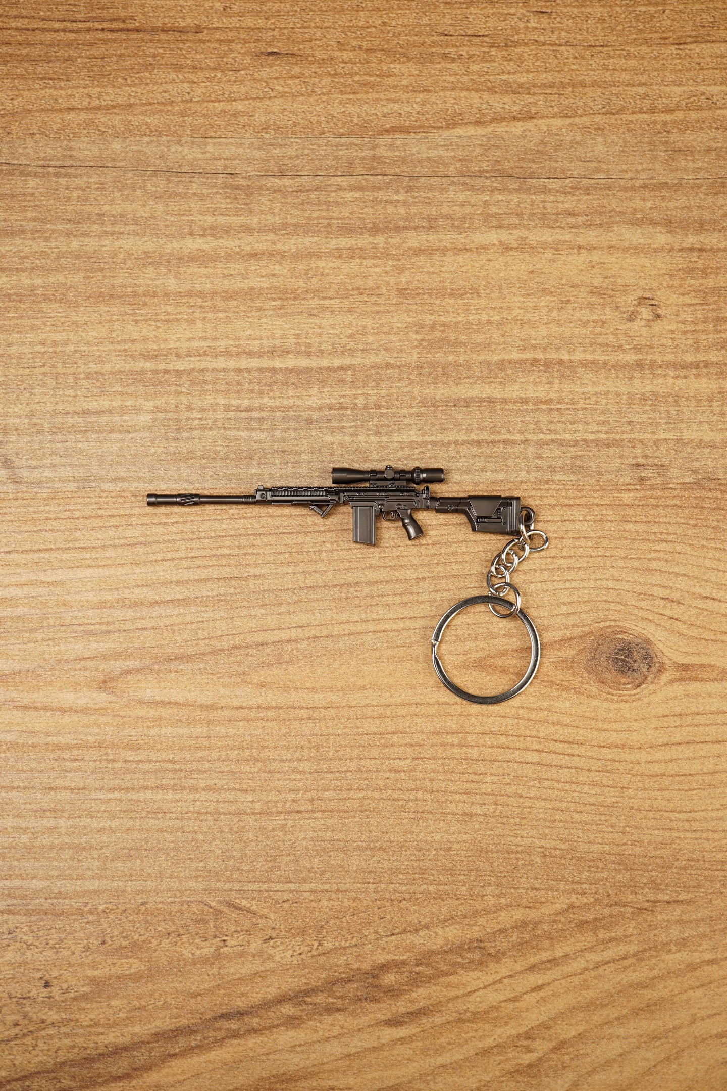 Modded SA58 FAL rifle keychain with scope-style detail, dark gunmetal finish and metal keyring attachment on wooden background
