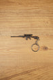 Modded SA58 FAL rifle keychain with scope-style detail, dark gunmetal finish and metal keyring attachment on wooden background