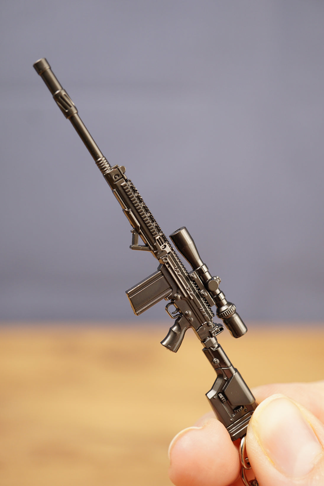 Close-up of modded SA58 FAL rifle keychain held upright, showing scope, rail detail, magazine and tactical stock design