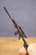 Close-up of modded SA58 FAL rifle keychain held upright, showing scope, rail detail, magazine and tactical stock design