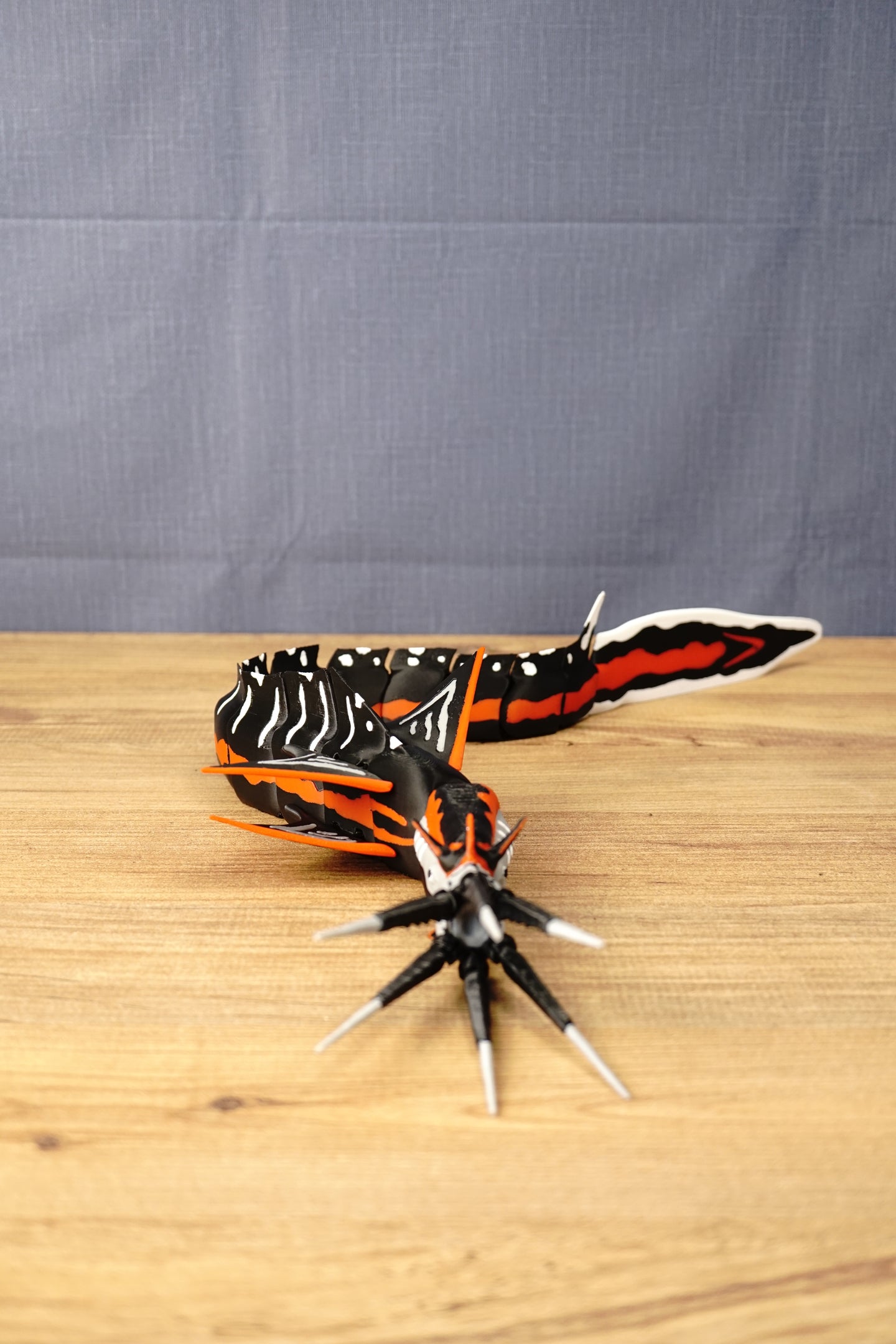 Needler Mango articulated display model posed on a wooden surface, showing its black, red and white segmented body, pointed tusks and detailed fins.