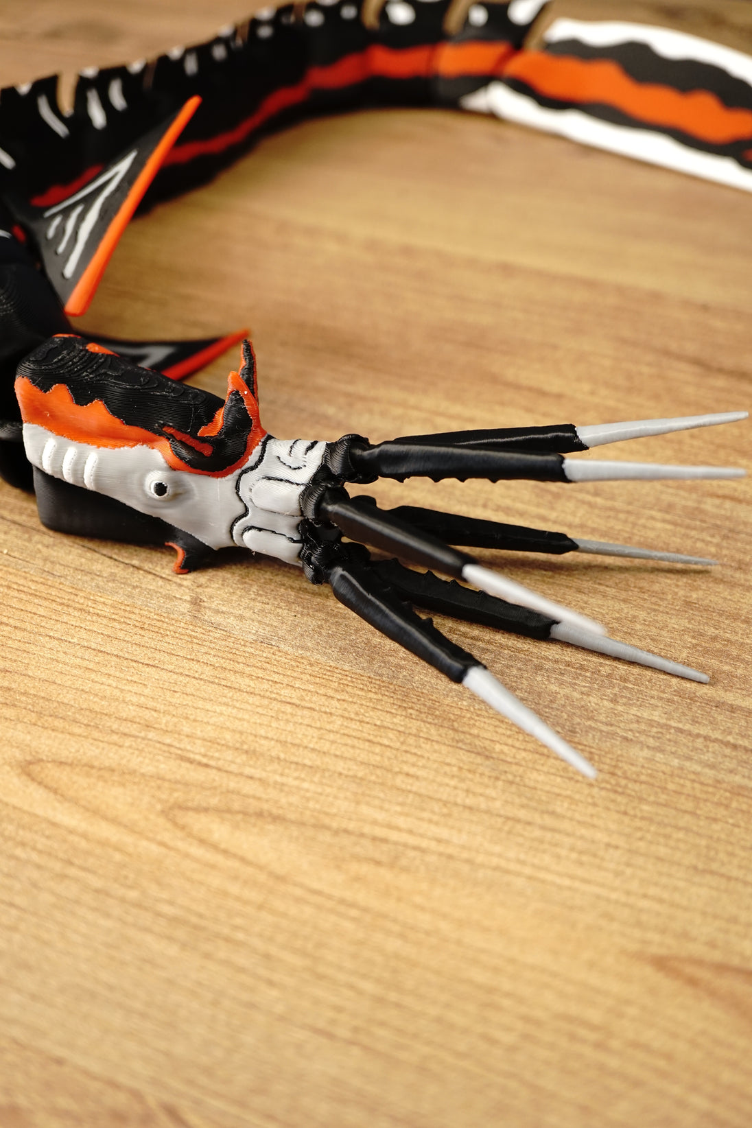 Close-up of the Needler Mango model’s articulated mouth and long tusk details, with a white face, black jaw sections and orange head markings.