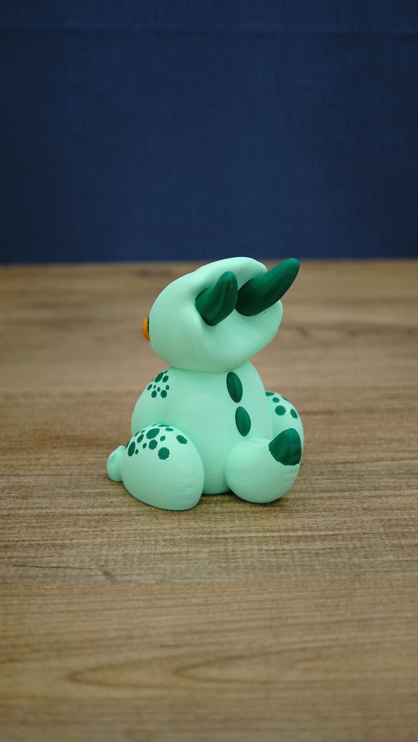Rear and side view of the Nibbles the Drake Palia collectible showing dark green horns, back markings, spotted legs and green tipped baby drake tail