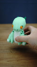 Nibbles the Drake Palia inspired figure held in a hand to demonstrate its compact collectible size, with orange eyes, green horns and white belly visible
